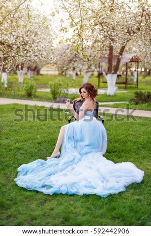 Portrait of beautiful young bride drinking champagne posing in the park or garden in blue dress outdoors on a bright sunny day green grass background