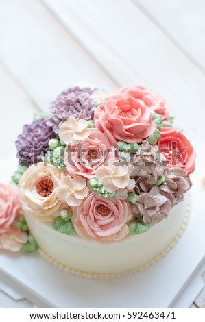 Gorgeous cake covered in roses made of butter cream icing on white wooden background