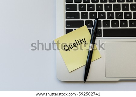 QUALITY word concept on sticky note, a pen and partial of laptop keyboard over top view flat lay isolated on white background.