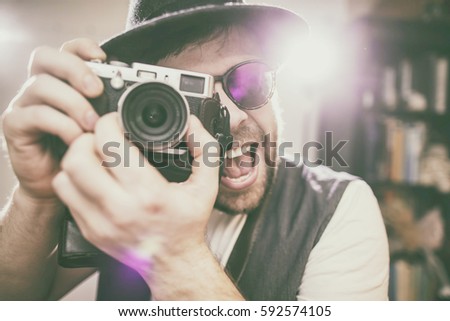 happy smiling photographer hipster wearing sunglasses and hat taking pictures using old style retro camera