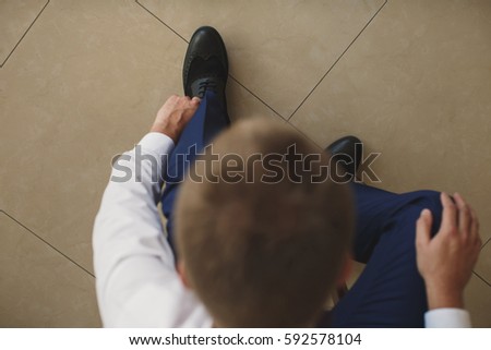 Man's hands tying shoelace of his new shoes. People, business, fashion and footwear concept - close up of man leg and hands tying shoe laces.