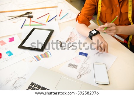 close up picture of woman designer using smartwatch touchscreen app connecting digital touch pad and smartphone online manufacturing office studio. profession and job occupation concept.