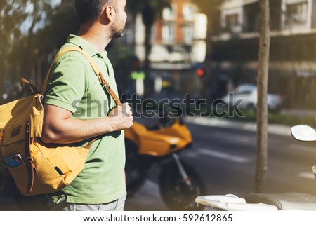 Hipster young man holding in hands backpack and map. Side view tourist traveler planning route on background sun and orange motorcycle. Person visiting city on backdrop summer street, mock up