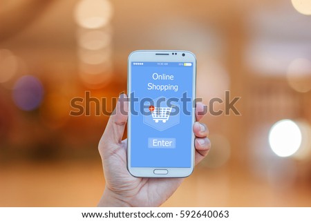 Hand holding smart phone with online shopping on screen over blurred in shopping mall background