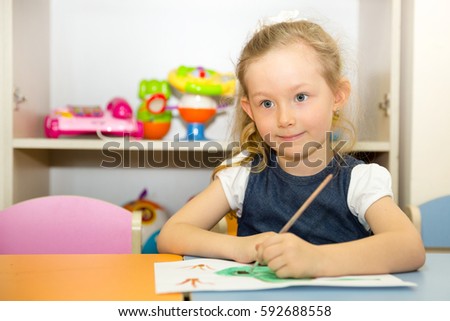Adorable child girl draws a brush and paints in nursery room. Kid in kindergarten in Montessori preschool class.