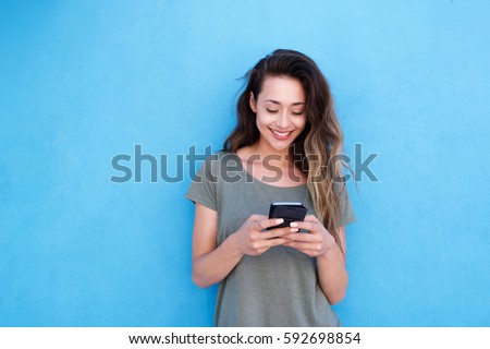 Front portrait of young smiling woman using mobile phone against blue background