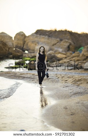 Young woman photographer holding camera and looking into frame. Girl dressed in black jumpsuit, European appearance. Concept of feminine beauty,  work photographer tourist with camera on vacation o