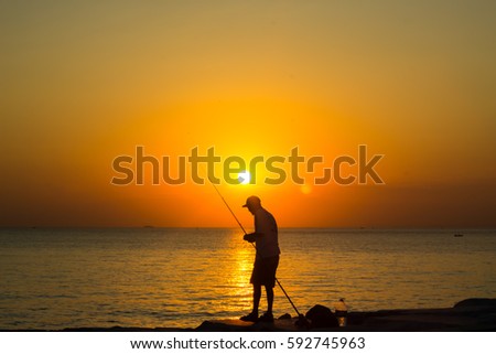 Man silhouetted fishing on the beach