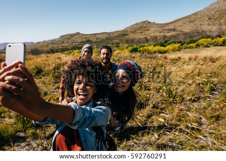Group of friends on walk taking selfie in countryside. Young people hiking in country taking self portrait with mobile phone.