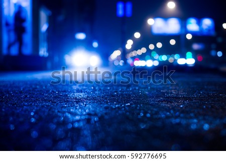 Rainy night in the big city, the car lights up the road and the man leaves home. Close up view from the sidewalk level, image in the blue tones