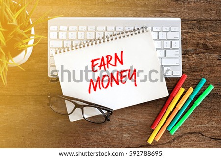 EARN MONEY Concept words on notebook with keyboard and glasses on rustic wooden table