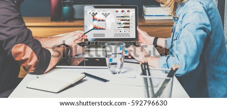 Meet one-on-one. Teamwork. Businesswoman and businessman sitting at table and looking at graphs, charts and diagrams on computer screen. Man shows pencil on computer monitor. Students learning online. Royalty-Free Stock Photo #592796630