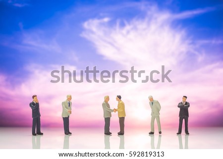 business miniature people make handshaking agreement on sunset sky background