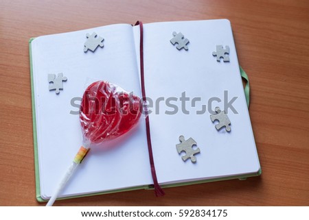 open notebook with bookmark on wooden table background. View from above. copy space, lollipop in the form of heart, puzzles, clip, decorative stone