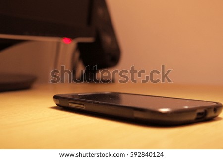Smartphone placed on wooden table near computer monitor and speakers in orange light toned.