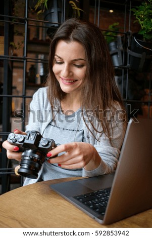Beautiful girl photographer is holding camera in her hands. Young woman looking at viewfinder and making photo in cafe.