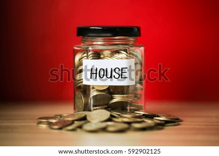 A lot coins in glass money jar with red background. Saving for house concept.