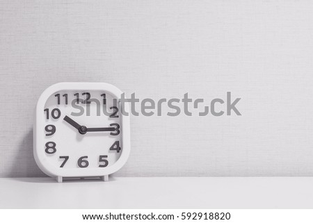 Closeup white clock for decorate show a quarter past ten or 10:15 a.m. on white wood desk and cream wallpaper textured background in black and white tone with copy space