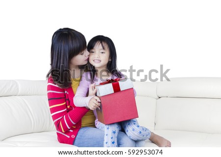 Portrait of young mother kisses her daughter cheek while holding a gift box, isolated on white background 