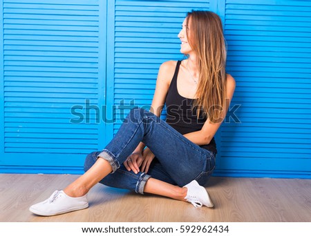 Hipster girl sitting on the floor against blue background.