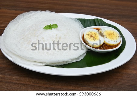 Appam / Palappam / plain hoppers made of white rice powder, a popular traditional Kerala breakfast bread with spicy masala egg curry on a houseboat, Alappuzha or Alleppey, India. South Indian food.