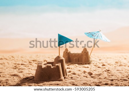 Sandcastles with a flag and an umbrella on the beach. Royalty-Free Stock Photo #593005205