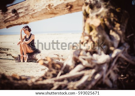 Ballerina in black dress sitting on the beach