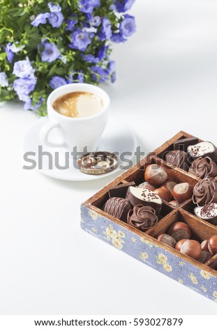 Cup of coffee on a white background with a variety of chocolates in a wooden box. Selective focus