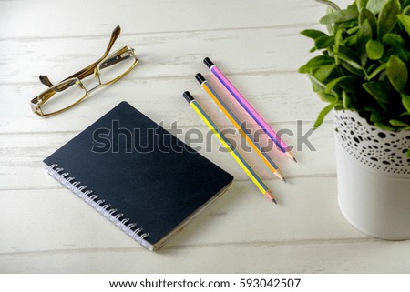 Book note with pencil, glasses and decorative plant on white wooden background.