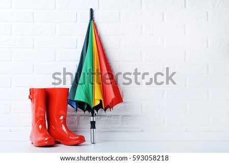 Red rubber boots with umbrella on brick wall background Royalty-Free Stock Photo #593058218
