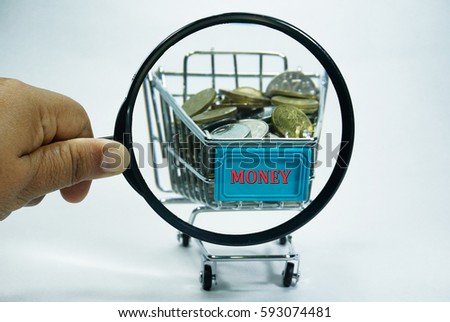 A hand holding a magnifying glass close up with a pile of coins currency of Malaysia  (MYR) in a trolley on isolated white background. A finance, saving and business concept. 