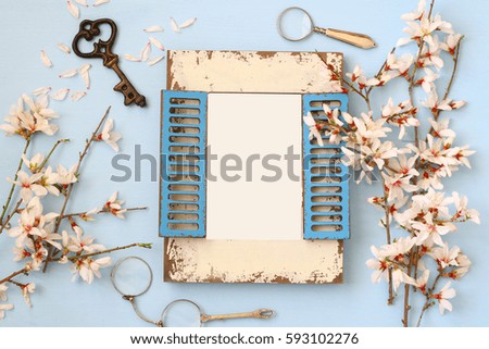 top view image of spring white cherry blossoms tree and blank photo frame on blue wooden background. Ready to put photography