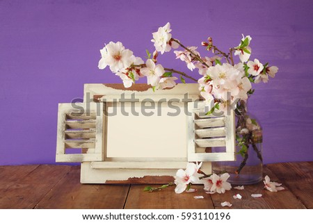Vintage blank photo frame next to spring white flowers on wooden table