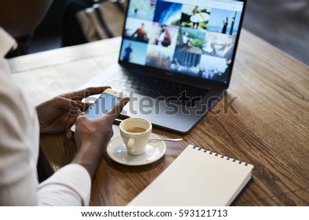 Cropped image of male hipster holding modern smartphone texting messages communicating through online chat with best friends arranging meeting during work break sitting in cafe with wifi zone