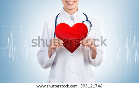 Young woman doctor against blue background holding red heart
