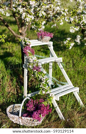 Garden decor - a wooden stairs with basket of lilacs on the background of blooming apple trees and greenery. The concept of spring flowers bloom in the parks