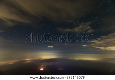 A view of earth atmosphere at night. Long exposure photography. The landscape shrouded in fast moving fog and clouds. Some star constellations can be seen through the clouds in the sky at night.