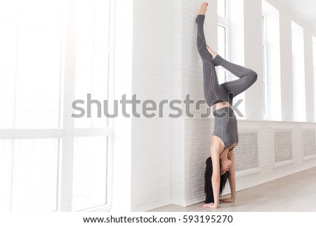 Sport and yoga. Strong young athletic woman doing exercise -Handstand against an picture window on black mat, full length