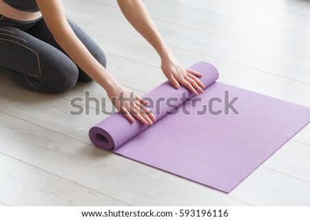 Young yoga Woman rolling her lilac mat after a yoga class on wooden floor near a window, close up Royalty-Free Stock Photo #593196116
