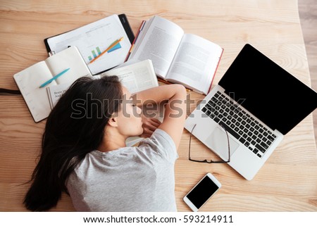 Photo of young tired caucasian woman sleeping on table indoors using laptop computer. Coworking concept.