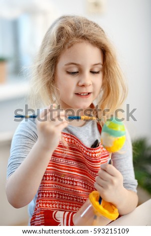 Little blonde girl coloring eggs for Easter holiday at home