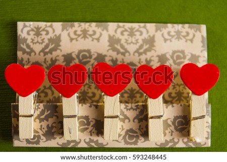Valentine's day concept. Red heart shape clothespins fixed on a cardboard with textured green background.