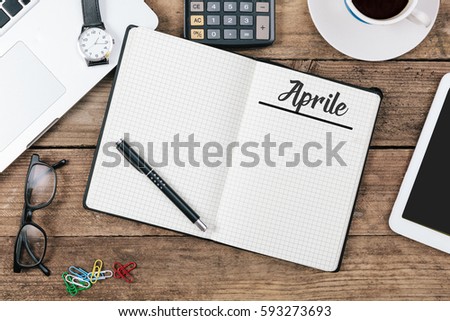 Aprile (Italian April) month name on notepad, office desk with electronic devices, computer and paper, wood table from above, concept image for blog title or header image.