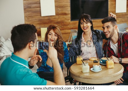 Young man photographing friends in a cafe with smartphone