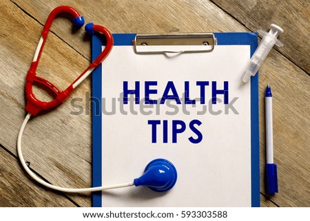 Healthcare concept. Stethoscope, syringe, pen and clipboard written with HEALTH TIPS on wooden background.