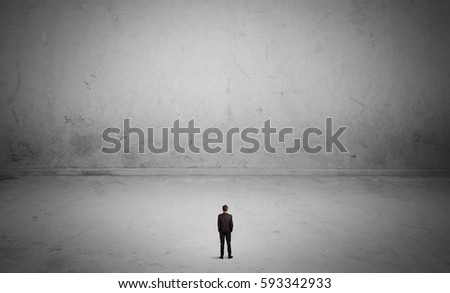 A tiny elegant businessman standing in large empty urban space with concrete walls and grey background concept