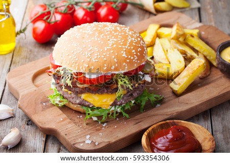 Burger, hamburger with french fries, ketchup, mustard and fresh vegetables on a cutting wooden board.