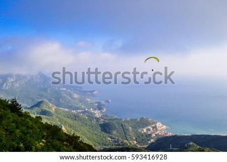 Man paragliding over Budva mountains overseeing sunny seaside Royalty-Free Stock Photo #593416928