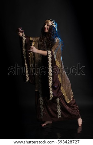 young girl with long hair in oriental dancer costume Khaleej posing and dancing on a black background in the scenic blue light