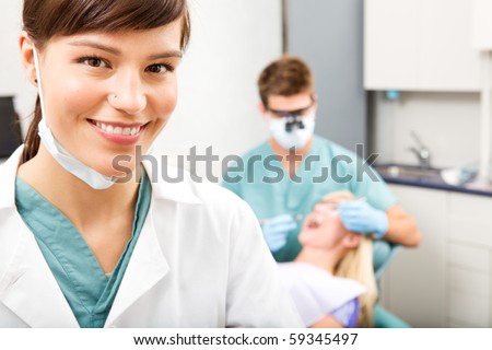 A portrait of a dental assistant smiling at the camera with the dentist working in the background Royalty-Free Stock Photo #59345497